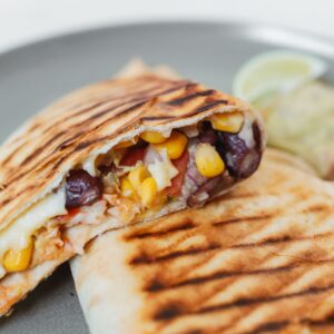 Delicious grilled quesadilla filled with beans, corn, and cheese, served on a plate.